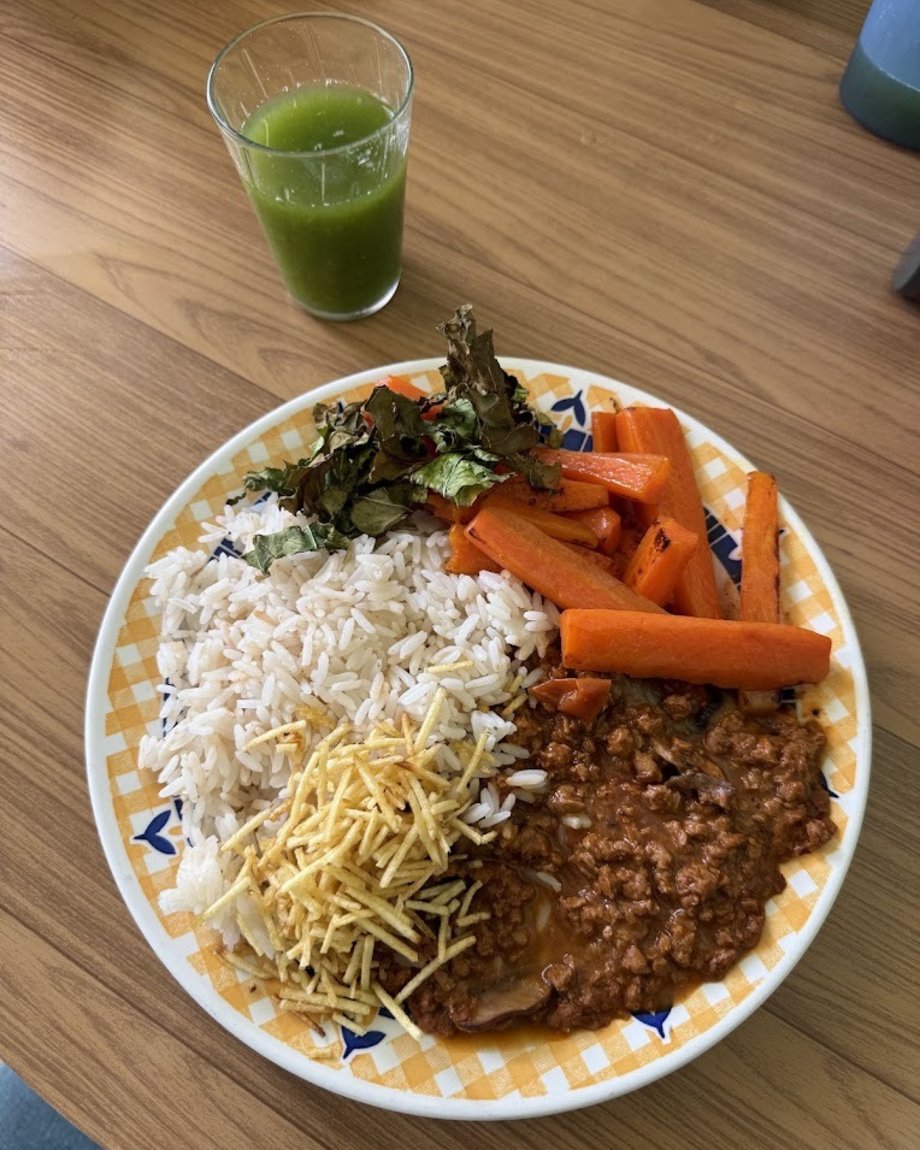 Prato com arroz, carne moída, cenoura assada e couve crocante, com suco verde ao lado